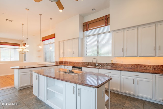 kitchen with white cabinets, a kitchen island, sink, pendant lighting, and dark stone counters