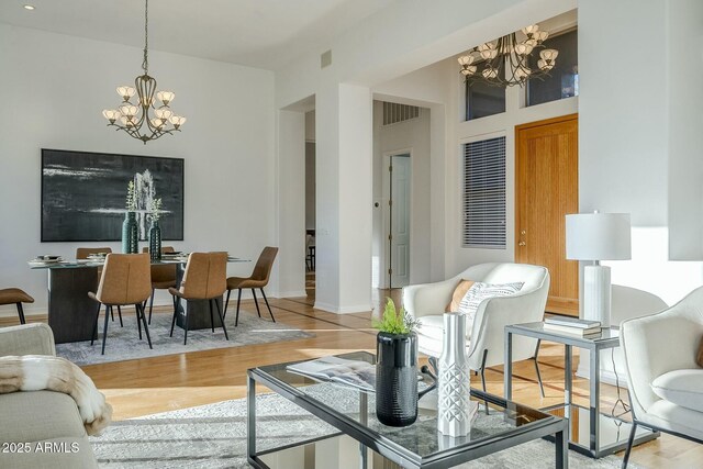 living room featuring baseboards, wood finished floors, visible vents, and an inviting chandelier