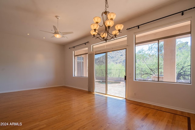 empty room with ceiling fan with notable chandelier, wood finished floors, and baseboards