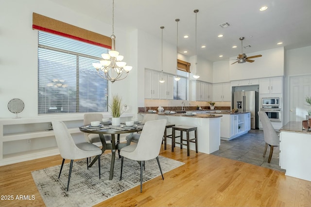 dining room featuring light wood finished floors, visible vents, a high ceiling, ceiling fan with notable chandelier, and recessed lighting