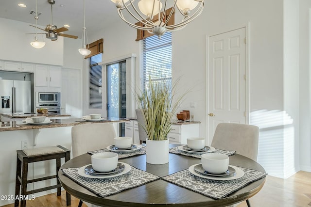 dining space with light wood-style floors, visible vents, a towering ceiling, and ceiling fan with notable chandelier