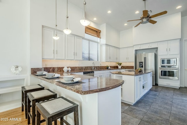 kitchen with a peninsula, appliances with stainless steel finishes, white cabinets, and a center island