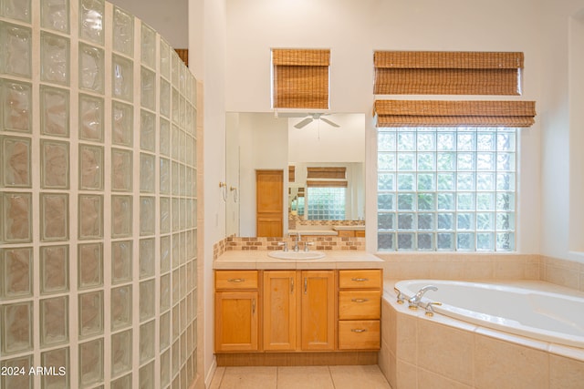 bathroom with tile patterned flooring, tiled tub, ceiling fan, and vanity