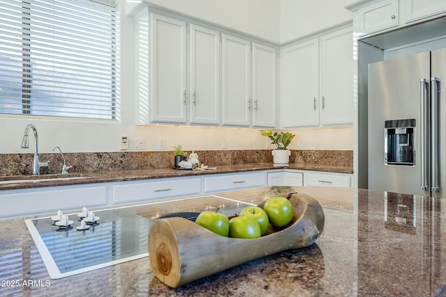 kitchen with a sink, high end refrigerator, white cabinetry, and dark stone countertops