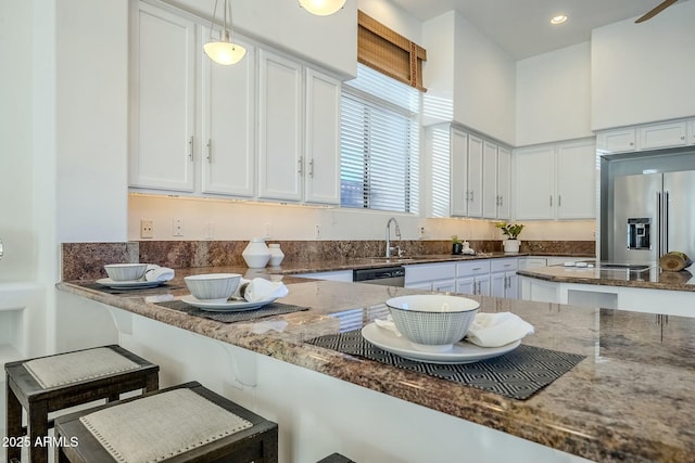 kitchen with stainless steel appliances, a sink, white cabinets, dark stone counters, and pendant lighting