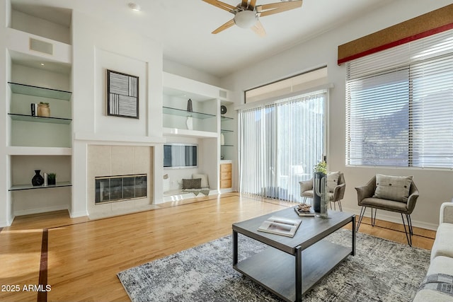 living room with baseboards, visible vents, built in features, a tile fireplace, and wood finished floors