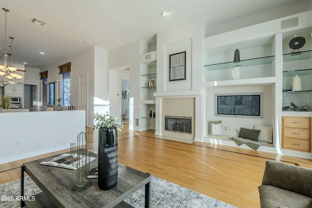 living area featuring an inviting chandelier, built in shelves, wood finished floors, and a tile fireplace