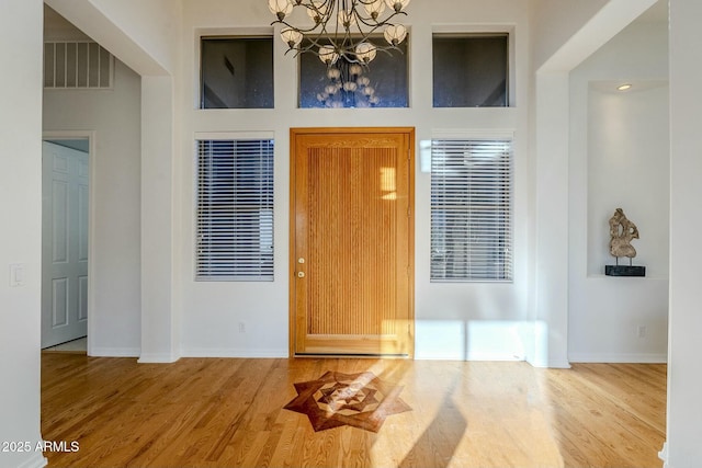 entrance foyer with a chandelier, wood finished floors, visible vents, and baseboards