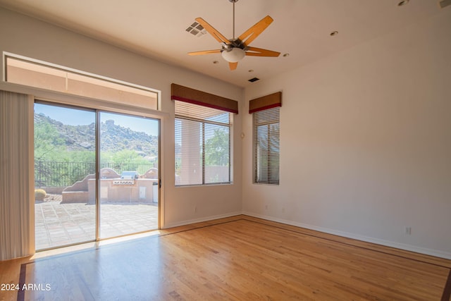 empty room featuring visible vents, light wood-style flooring, a mountain view, and a healthy amount of sunlight