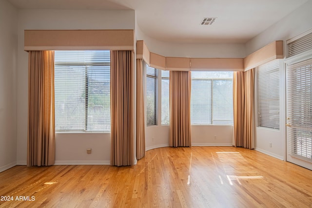 empty room featuring baseboards, light wood-style flooring, visible vents, and a wealth of natural light