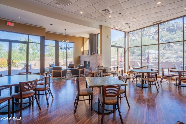 dining room featuring a notable chandelier, expansive windows, a brick fireplace, and dark wood-type flooring