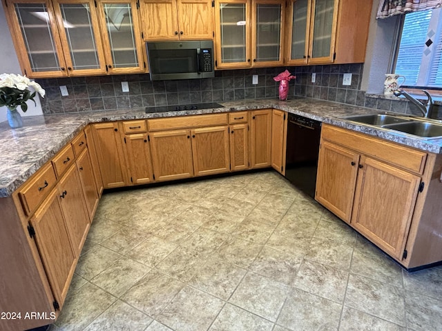 kitchen featuring tasteful backsplash, glass insert cabinets, a sink, brown cabinets, and black appliances