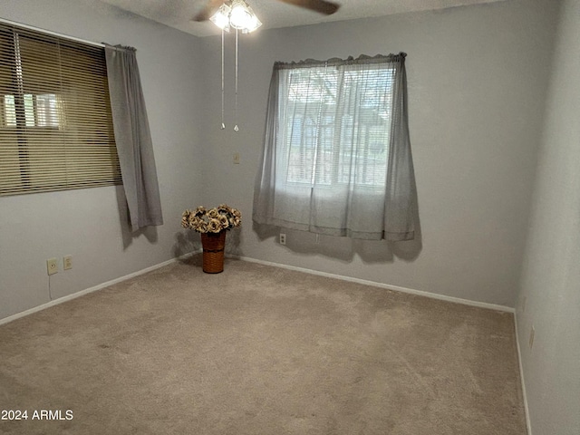 carpeted spare room featuring baseboards and a ceiling fan