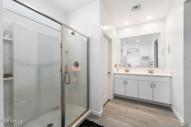 full bathroom featuring wood finish floors, visible vents, a sink, a shower stall, and double vanity