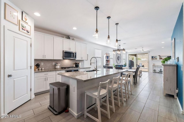 kitchen with a sink, stainless steel microwave, backsplash, white cabinets, and stove