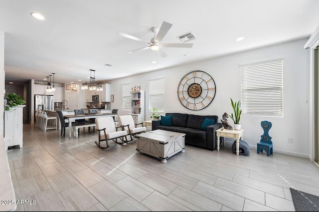 living area featuring recessed lighting, visible vents, ceiling fan with notable chandelier, and baseboards