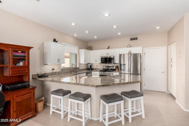 kitchen with a breakfast bar, sink, kitchen peninsula, stainless steel appliances, and white cabinets