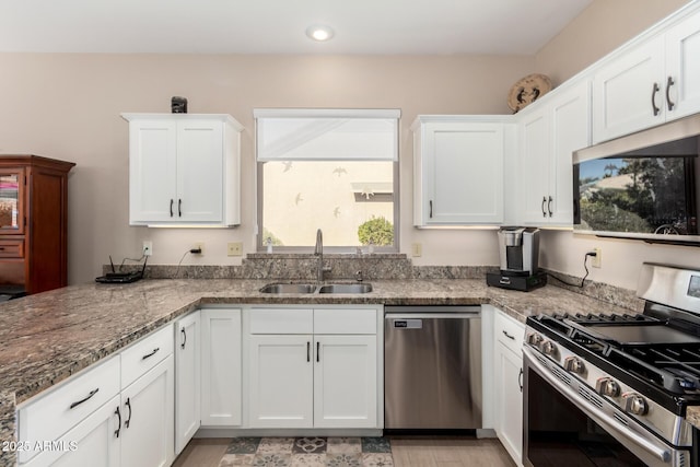 kitchen featuring appliances with stainless steel finishes, sink, white cabinets, kitchen peninsula, and light stone countertops