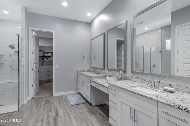 full bath featuring vanity, a shower stall, a walk in closet, and wood finish floors