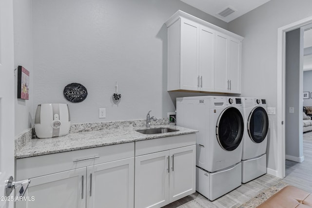 laundry area with washing machine and clothes dryer, visible vents, wood tiled floor, cabinet space, and a sink