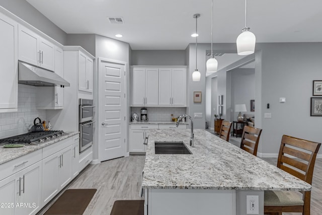 kitchen featuring visible vents, light wood-type flooring, under cabinet range hood, a sink, and stainless steel appliances