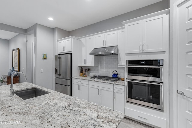 kitchen with under cabinet range hood, decorative backsplash, appliances with stainless steel finishes, white cabinets, and a sink