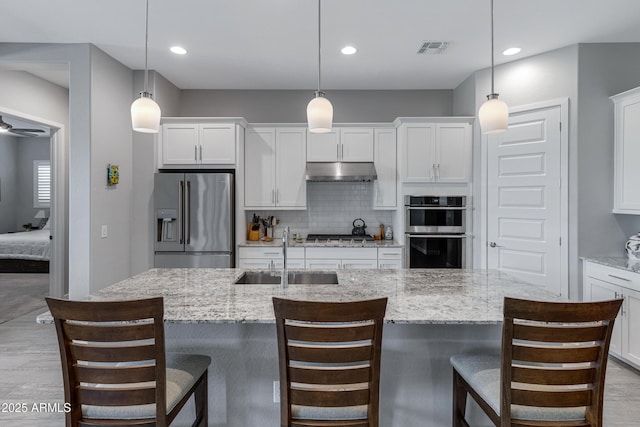 kitchen featuring visible vents, a sink, stainless steel appliances, under cabinet range hood, and tasteful backsplash