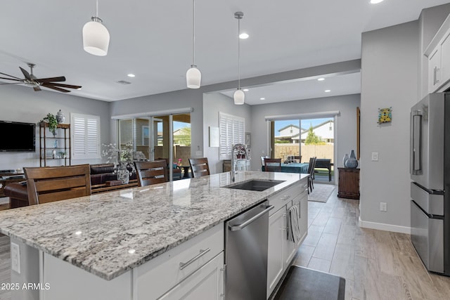 kitchen featuring light wood-style flooring, a ceiling fan, a sink, open floor plan, and appliances with stainless steel finishes