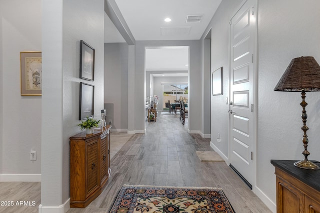 hall with visible vents, baseboards, and light wood-style flooring
