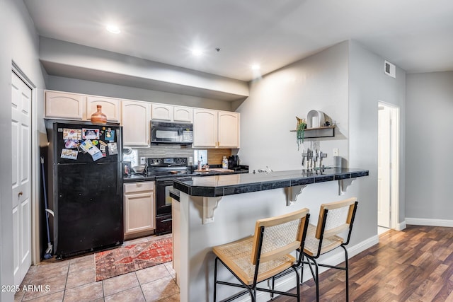 kitchen with tasteful backsplash, visible vents, a kitchen breakfast bar, a peninsula, and black appliances