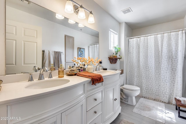 bathroom with double vanity, visible vents, toilet, and a sink