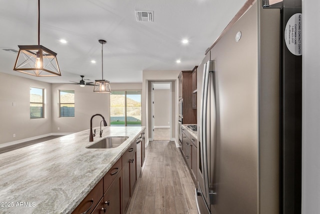 kitchen featuring sink, light stone counters, pendant lighting, stainless steel appliances, and light hardwood / wood-style floors