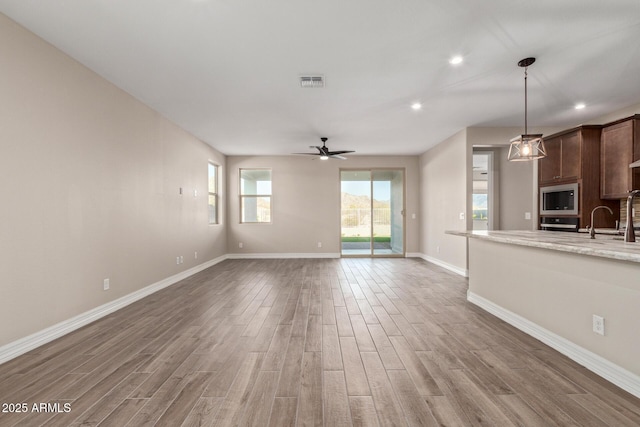 unfurnished living room featuring ceiling fan, wood-type flooring, and sink