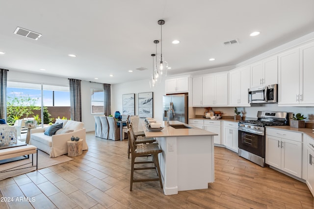 kitchen featuring hanging light fixtures, an island with sink, light hardwood / wood-style floors, white cabinetry, and stainless steel appliances