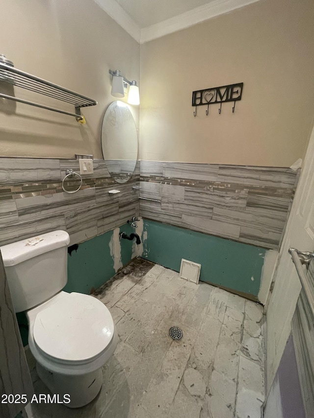 bathroom featuring crown molding, toilet, and tile walls