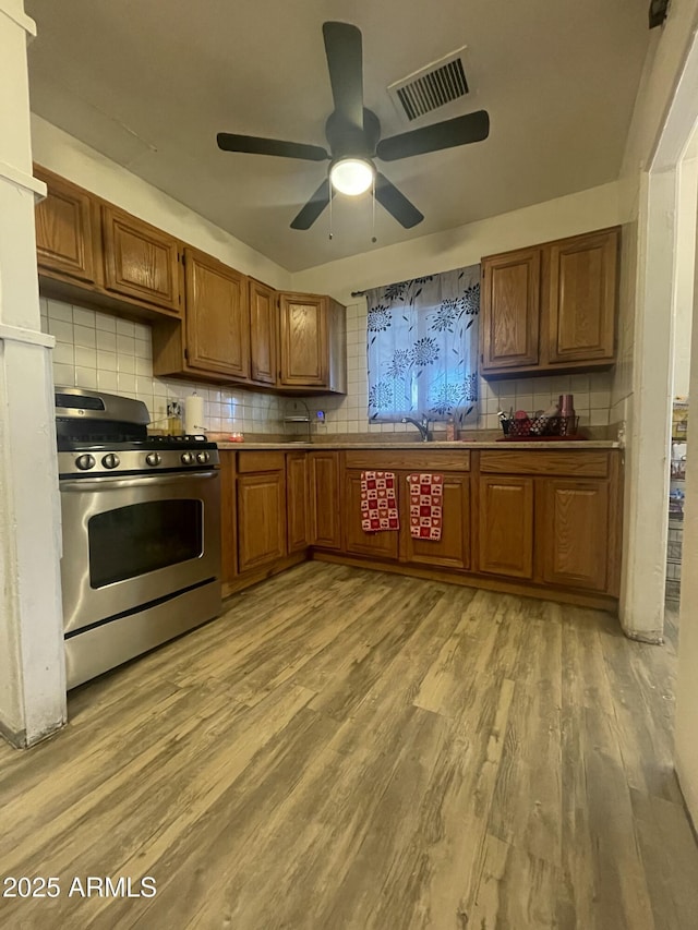 kitchen featuring decorative backsplash, stainless steel gas range, and light hardwood / wood-style flooring