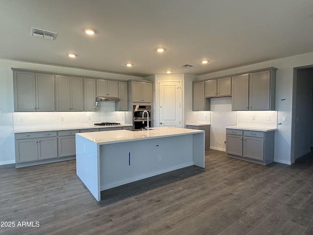 kitchen with a center island with sink, visible vents, light countertops, and gray cabinetry