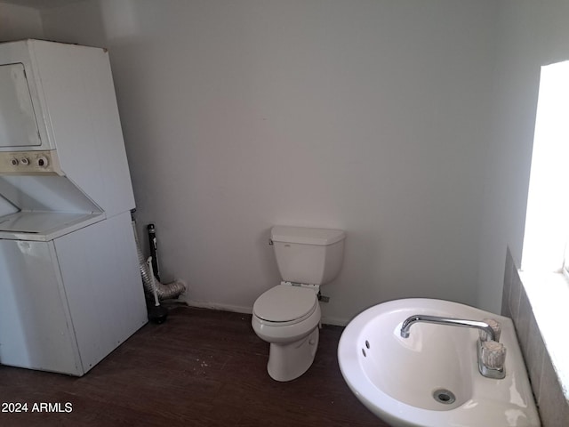 half bath with toilet, stacked washing maching and dryer, baseboards, and wood finished floors