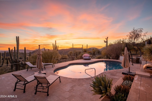 pool at dusk with a mountain view, fence, a fenced in pool, and a patio area