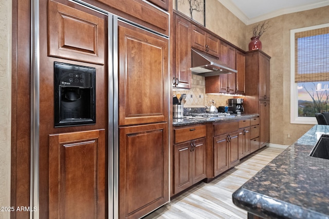 kitchen with light wood finished floors, ornamental molding, gas cooktop, dark stone countertops, and under cabinet range hood