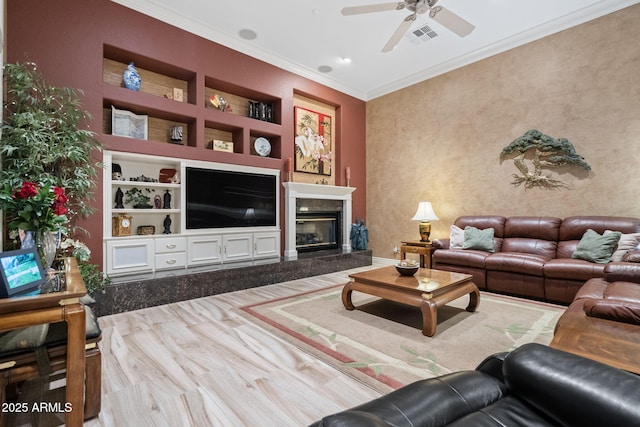 living room with built in features, crown molding, a fireplace, visible vents, and a ceiling fan