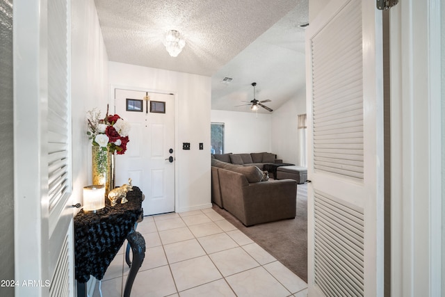 foyer entrance with a textured ceiling, ceiling fan, light tile patterned floors, and vaulted ceiling