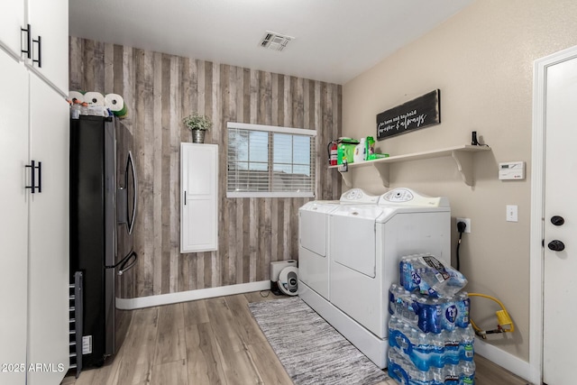 washroom featuring washing machine and clothes dryer, light hardwood / wood-style floors, and wood walls