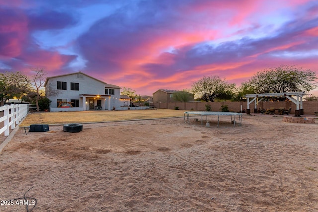 yard at dusk featuring a trampoline and a pergola