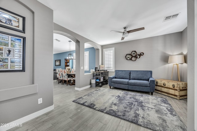 living room featuring ceiling fan with notable chandelier and light hardwood / wood-style floors