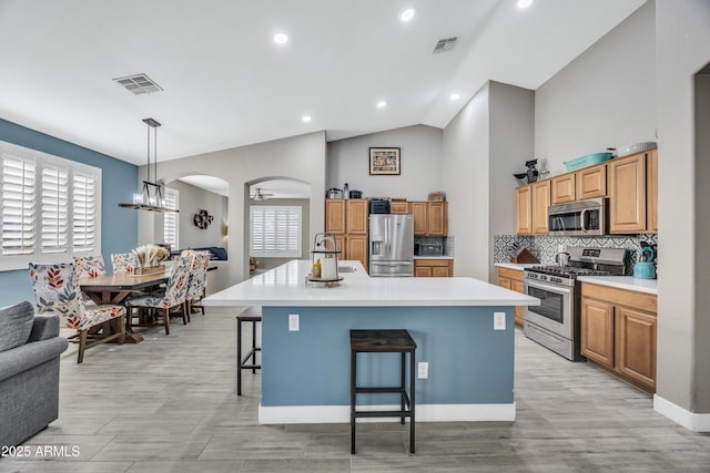 kitchen with ceiling fan, stainless steel appliances, an island with sink, decorative light fixtures, and a breakfast bar