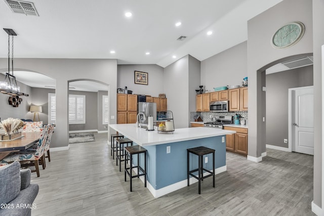 kitchen featuring pendant lighting, a spacious island, appliances with stainless steel finishes, light hardwood / wood-style floors, and a kitchen bar