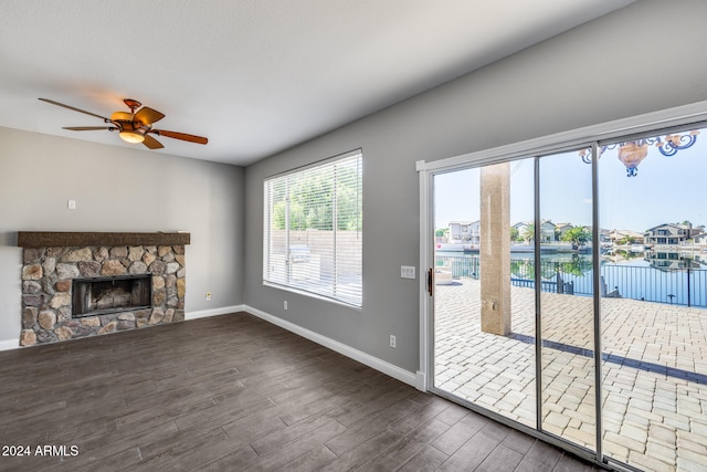 unfurnished living room featuring a water view, a stone fireplace, dark hardwood / wood-style floors, and ceiling fan