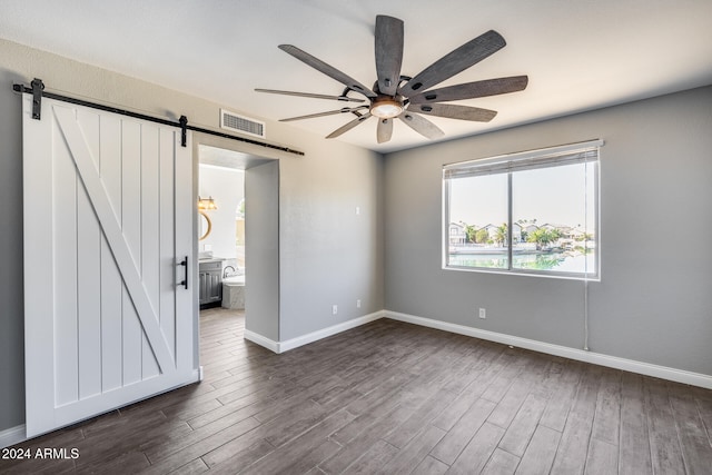 empty room featuring ceiling fan, dark hardwood / wood-style floors, and a barn door