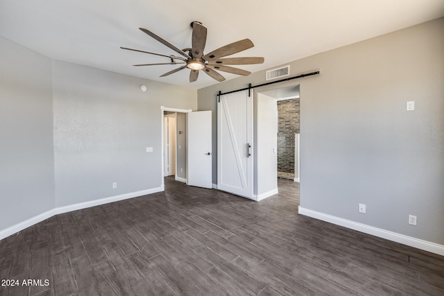 unfurnished bedroom featuring ceiling fan, dark hardwood / wood-style flooring, and a barn door